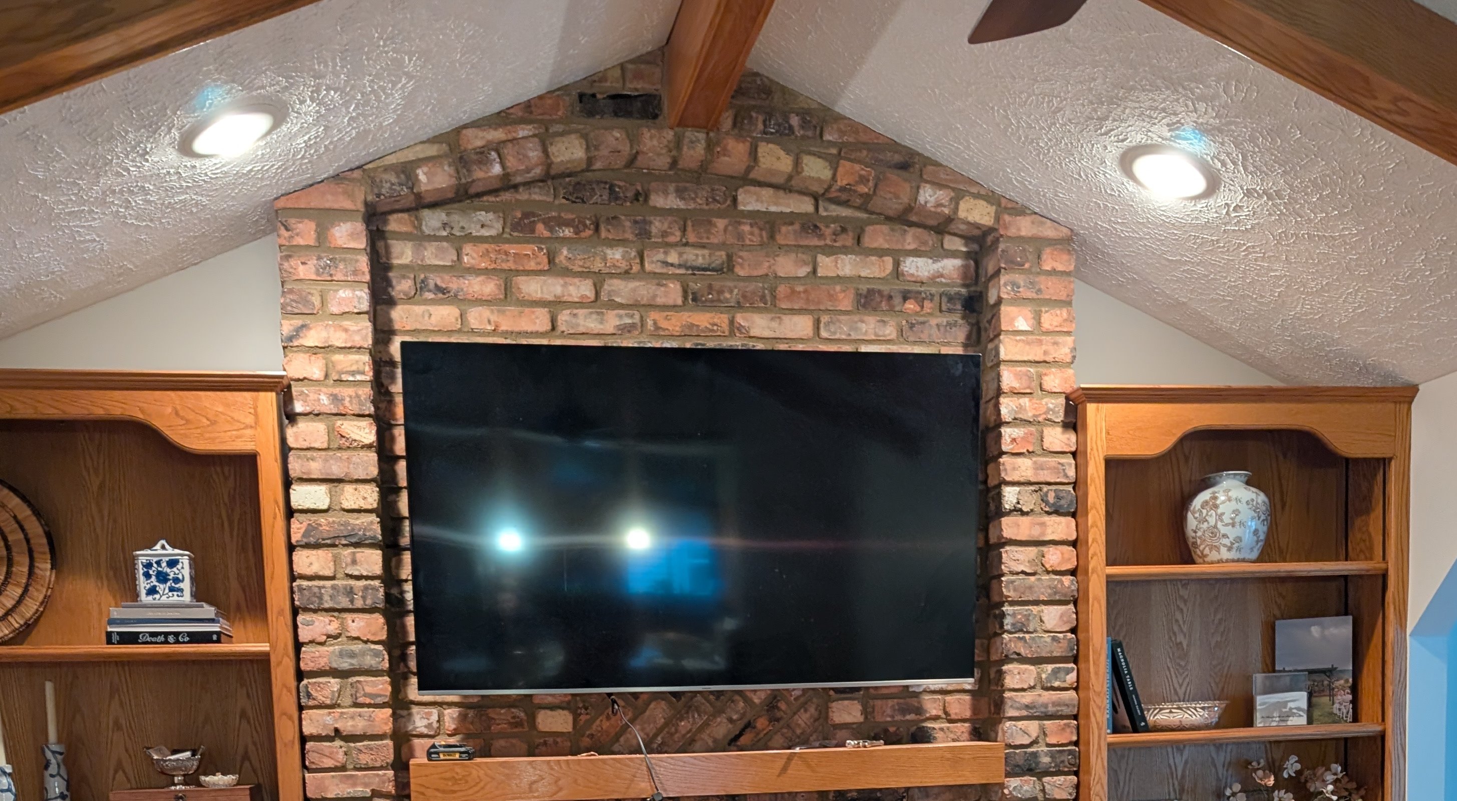 a flat-screen TV mounted on a brick fireplace between oak built-in shelves.